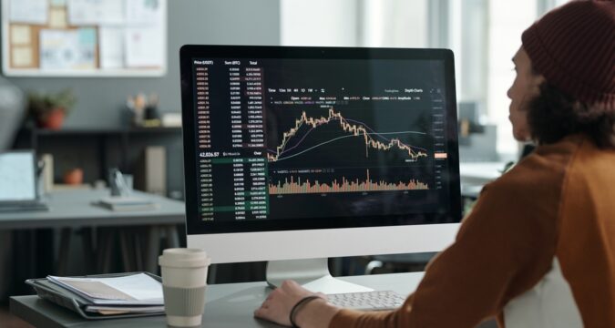 MaleAnalystSittingInFrontOfComputerMonitorWithGraph | Cryptocoin Stock Exchange Reseña de Quintustrade (quintustrade.com) – Afilando tu Ventaja en el Trading con Esta Plataforma